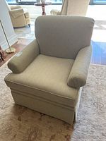 Front angle view of beige upholstered swivel lounge chair showing cushion, arms, and skirt details.
