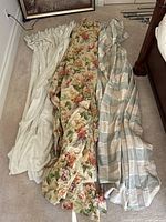 Three sets of curtains laid out on floor showing colors and patterns: off-white, floral, and grey checkered.