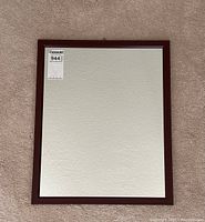 Front view of square mirror with dark brown faux wood frame on carpeted floor