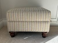Front view of striped fabric upholstered ottoman showing striped pattern and turned wooden legs.
