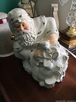 Side view of large Santa cookie jar dressed in white with holly decorations holding a bag of toys, showing detailed face and beard.