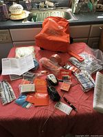 Full view of the orange emergency kit opened with items laid out on a pink cloth, including flashlight, food pouches, emergency blanket, batteries, and walkie talkie.