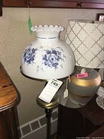 Full view of brass floor lamp featuring the blue floral glass shade with scalloped edge on a brass base.