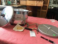 Dough Girl Bread Maker aluminum pot with lid, crank handle, an instruction sheet, and additional metal parts on a red tablecloth.