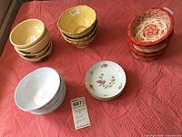 Photo showing various small bowls arranged in sets on a pink fabric surface, including yellow, orange, cream, floral and white bowls.