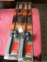 Pair of two new Diawa fishing rods in original packaging on pink blanket, showing cardboard backing with Diawa brand and rods equipped with spinning reels.
