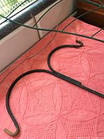 Curved metal hooks of the double plant hanger shown laying flat indoors on a towel, green paint with some wear visible