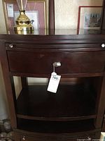 End table with dark wood stain, curved front drawer, and metal handles, showing full piece from front.