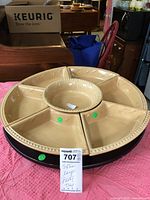 Full view of the extra large beige ceramic dishes sitting in a dark wooden circular base lazy Susan on a pink cloth with parts of furniture and boxes visible in background.
