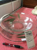 Clear top view of large glass bowl with leaf motif and matching underplate, pen included for scale.