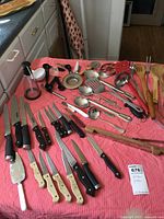 Full view of kitchen items spread on pink cloth including knives, wooden utensils, ladles, and scoops.