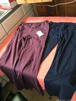 Two pairs of ladies' full stretch pants lying flat on a bed, navy blue pair by Safort on the right and burgundy heather pair by Yugo on the left.