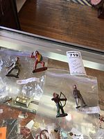 Four tin soldier and Native American figurines in plastic bags, displayed on glass countertop