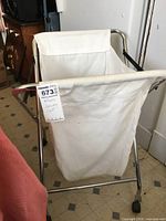 Laundry cart with folding metal frame and tan cloth bag on wheels, approximate dimensions noted as 29 inches height by 17 inches width.