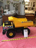 Full side view of the large yellow and black metal Tonka dump truck on a pink textured surface with measuring tape showing length.