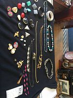 Full view of mixed costume jewelry laid out on black fabric, includes necklaces, bracelets, earrings, pins, pendant, showing variety of styles.