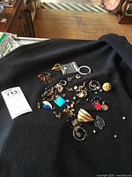 Loose jewelry pieces spread on black fabric showing assortment of rings, earrings, brooch, and beads