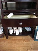 Nightstand showing drawer open with metal handle, bottom shelf holding several cylindrical objects, and pull-out shelf above drawer.