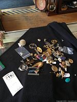 Photo of the mixed lot of pins and brooches spread on a black surface, showing various styles and colors in metal and enamel.