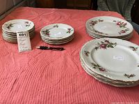 Set of small, medium, and dinner plates arranged on a table with pink cloth showing floral rose pattern and gold accents
