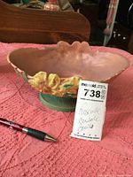 Roseville console bowl on pink quilted fabric, showing side view with yellow flowers and green base, pen for scale, and lot tag.
