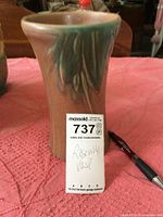 Roseville vase showing the raised leaf design and shape, sitting on pink cloth with pen and auction tag for scale.