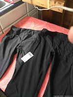 Two pairs of stretch pants by Yugo laid on a red bedspread. One pair is gray melange, the other is black.