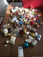 Photo showing large assortment of Christmas ornaments spread on a tabletop with varying shapes and colors and a red box in the background.