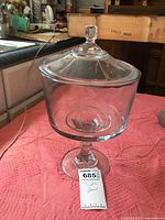 Full view of clear glass trifle bowl with lid on pink cloth background.