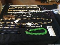 Top view of various beaded necklaces laid out on a black cloth, showing lengths with measuring tape and variety of bead types and colors.
