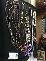 Top-down view of 11 assorted costume necklaces on a black background, showing a variety of beads and chain styles, along with a measuring tape indicating length.