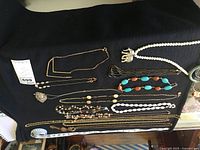 View of multiple costume necklaces including chains, bead necklaces, and stone necklaces laid out on a black cloth. Notable elephant pendant on white bead necklace seen.