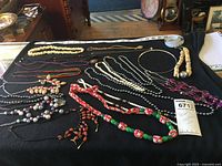 Wide view of multiple assorted costume necklaces laid out on a black cloth, showing different materials and colors.