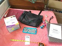 Photo showing all items together on a red mattress including Netgear box, car trash tote bag, remote holder, bumper sticker, flashlights, Verizon battery holder, monoscope, tape and measuring tape.