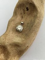 Photo of the moissanite pendant displayed on a wooden textured surface showing the solitaire gemstone and bail.