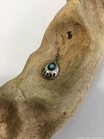 Front view of small silver bear paw pendant showing turquoise stone in center, laying on a piece of wood.