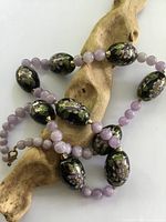 Close-up photo of the cloisonné and purple stone beads laid on a piece of driftwood to show bead details and color.