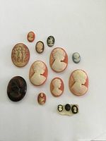 Top view of eleven faux antique cameos ranging in size, color, and design placed on white background.