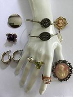 Photo showing all vintage jewelry items including cameo brooches, bracelets, rings, hoop earrings, flower pin, and round brooch displayed on a white mannequin hand and flat surface