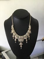 Front view showing filigree work, rectangular and oval links, central pendant with hanging tassels on black bust