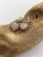 Pair of sterling silver drop earrings with heart-shaped rose quartz stones displayed on a textured wooden surface.
