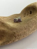 Pair of sterling silver stud earrings with round purple amethyst stones resting on a wooden display.