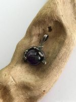 Front view of vintage sterling silver turtle pendant holding a moveable deep purple amethyst bead, placed on a natural wood surface.