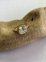 Front angled view of the gilt sterling silver engagement ring showing the large crystal center stone and band detail resting on a wooden textured display.
