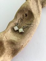 Pair of sterling silver drop earrings with square mother of pearl inlays placed on a natural wood surface.