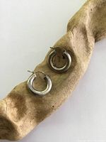Pair of rounded sterling silver hoop earrings on a wooden textured prop, showing lever clasp closures and surface wear.