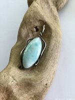 Sterling silver pendant with blue stone resting on textured wooden background.