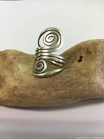 Front view of sterling silver double spiral ring balanced on a piece of light brown wood, showing the size and spiral design