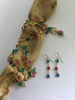 Necklace and earrings laid on wooden display showing multicolored crystal beads in gold-tone settings.