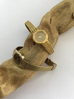 Photo of two vintage women's gold tone wristwatches on a piece of driftwood, showing overall design and condition.